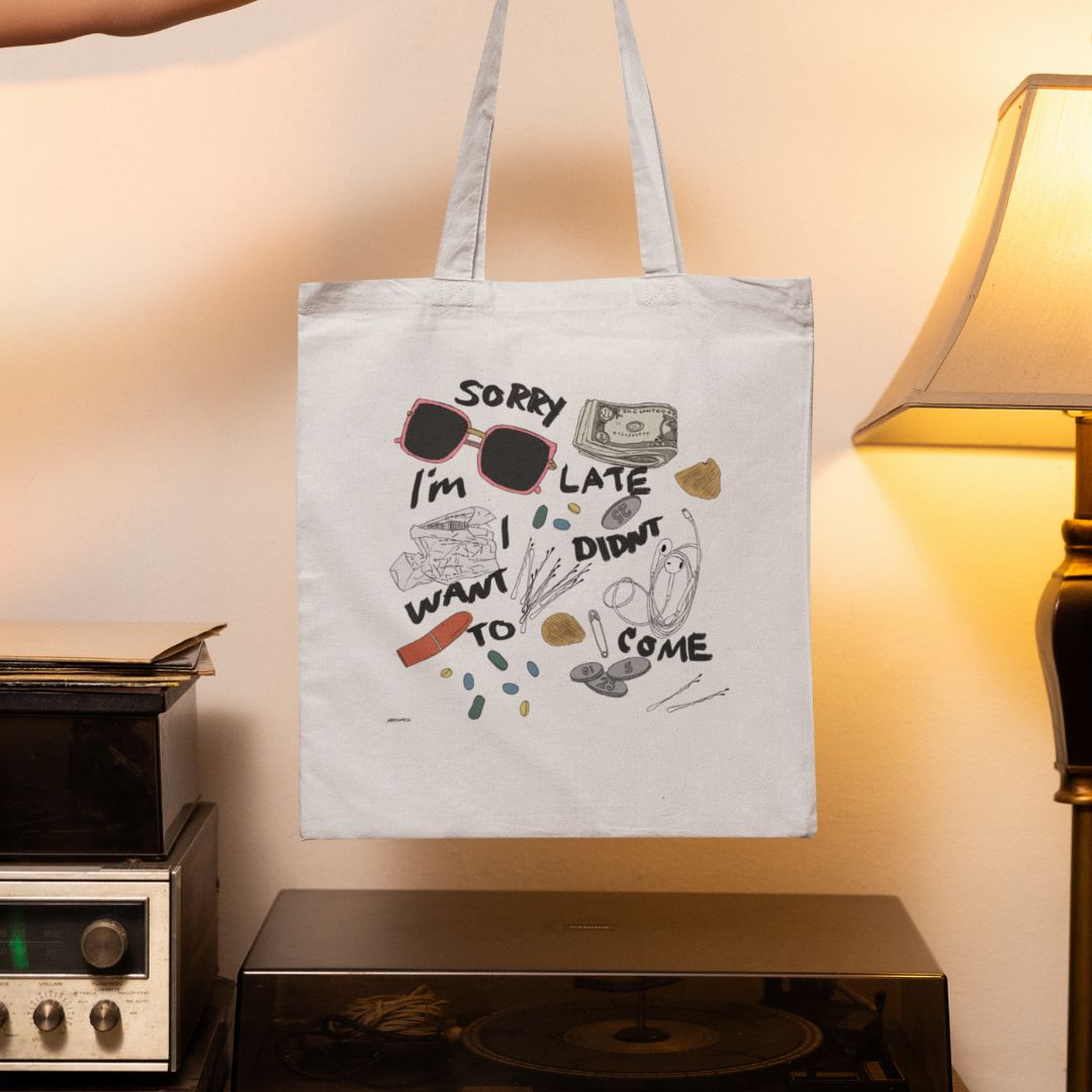 A hand holds a white tote bag with doodles, sunglasses, pills, a dollar bill, and the text Sorry Im late, I didnt want to come, above a stereo and beside a lit lamp.