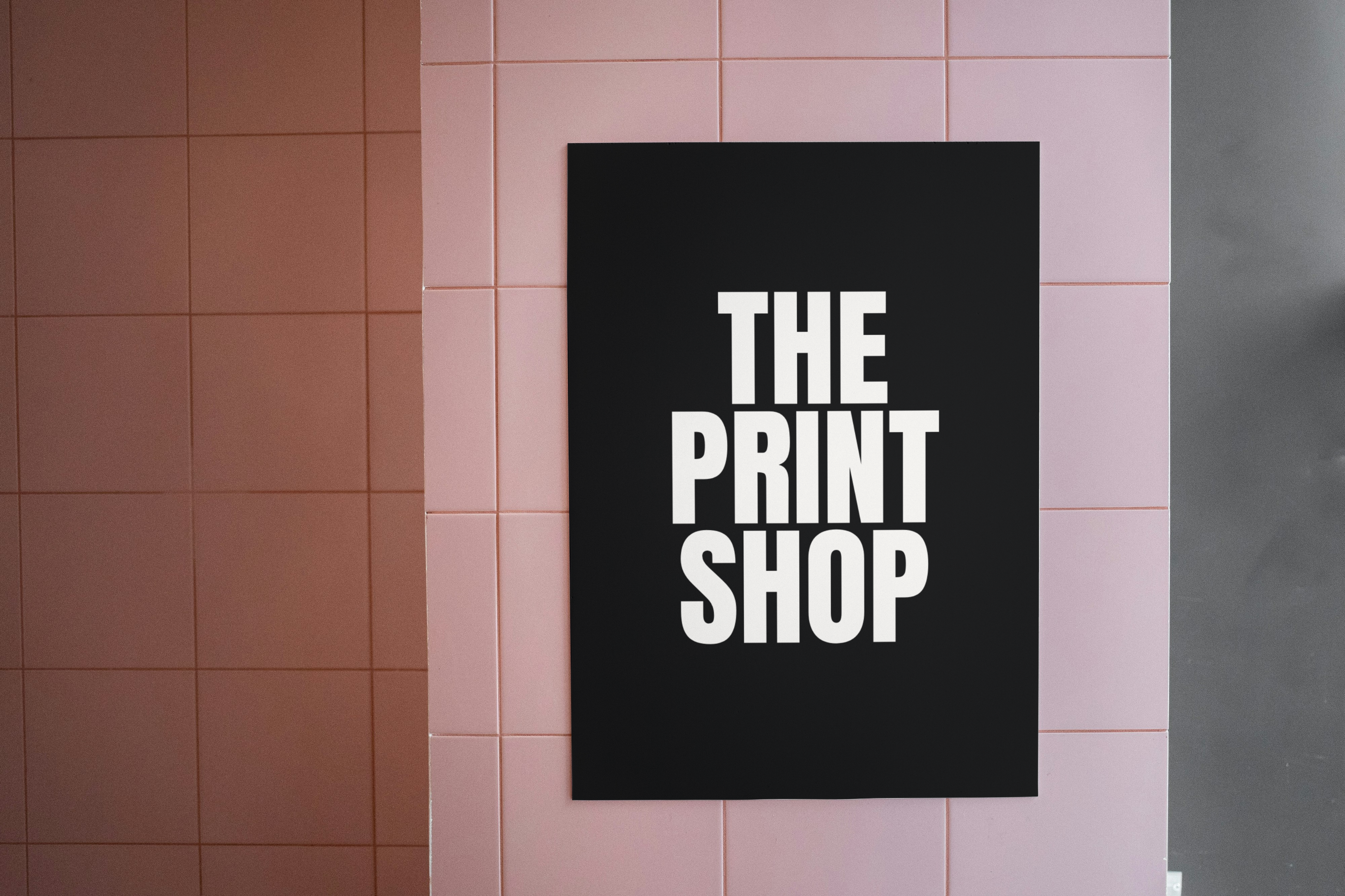Black sign with 'THE PRINT SHOP' text on a pink tiled wall.